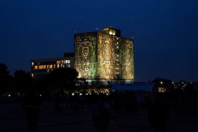 Vista nocturna de la Biblioteca Central de la UNAM iluminada, referente cultural y académico que acompaña los esfuerzos de la universidad en emprendimiento científico e innovación.