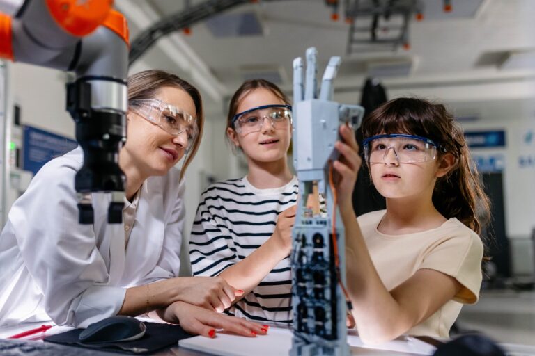 Docente guía a dos estudiantes en la construcción de una mano robótica durante una actividad STEM, fomentando equidad y sostenibilidad en la educación secundaria.