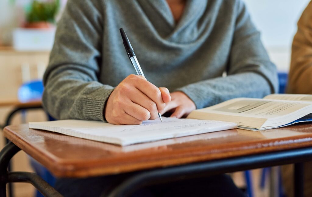 Estudiante escribe en cuaderno con libro abierto, reflejando los retos tras la retirada de normativas de educación federal que protegían a estudiantes de inglés.