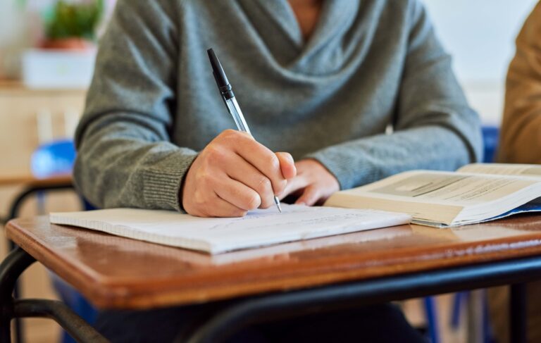 Estudiante escribe en cuaderno con libro abierto, reflejando los retos tras la retirada de normativas de educación federal que protegían a estudiantes de inglés.