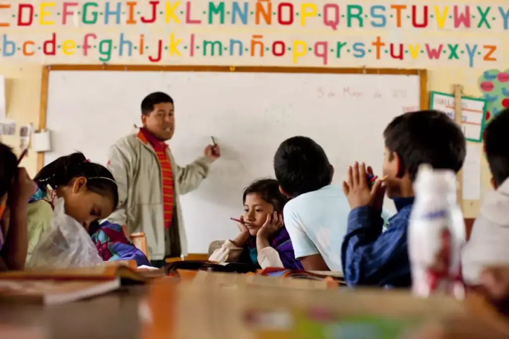 Niños de comunidades indígenas aprendiendo en su lengua materna y español en un aula de primaria que representa la educación bilingüe.