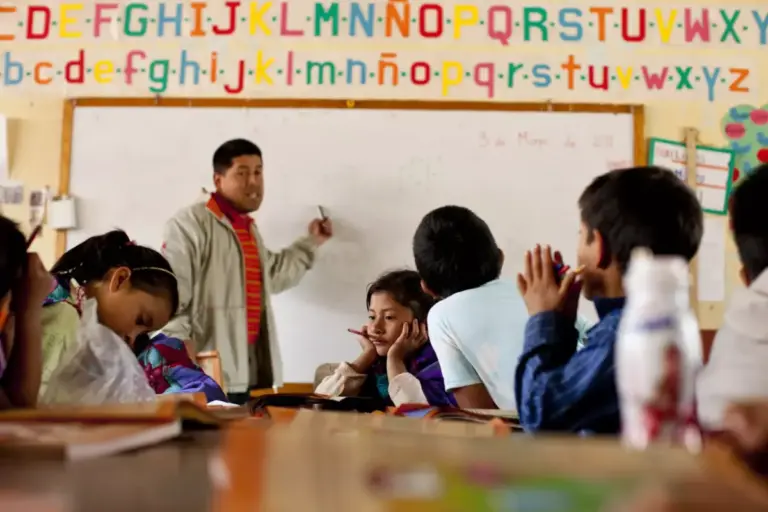 Niños de comunidades indígenas aprendiendo en su lengua materna y español en un aula de primaria que representa la educación bilingüe.