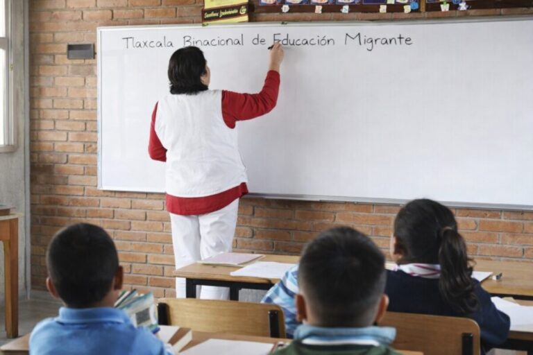 Docente escribe en pizarrón frente a estudiantes en aula de Tlaxcala como parte del programa de educación migrante