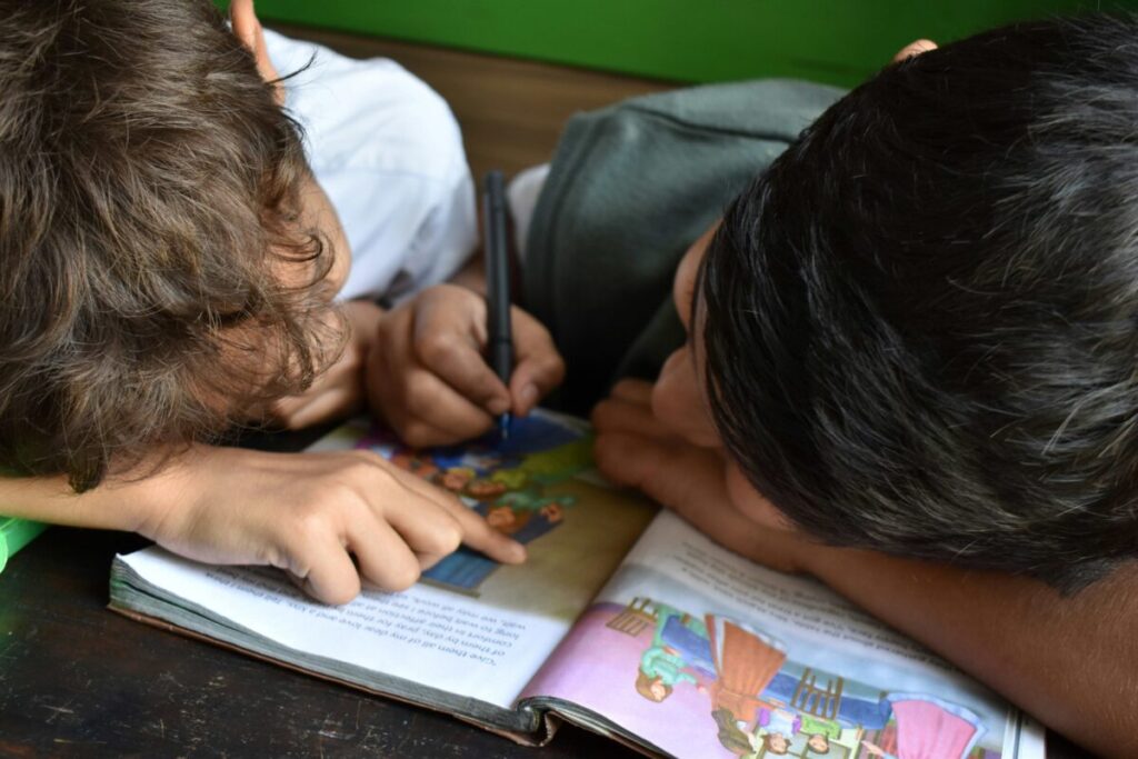 Grupo de niños pequeños leyendo libros en aula con apoyo docente como parte de una política de alfabetización inicial