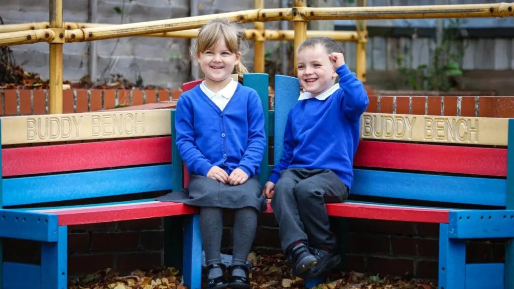 niños pequeños en uniforme escolar sentados en banco de amistad en patio, reflejando entorno de educación inicial y convivencia escolar positiva