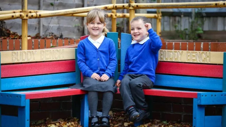 niños pequeños en uniforme escolar sentados en banco de amistad en patio, reflejando entorno de educación inicial y convivencia escolar positiva