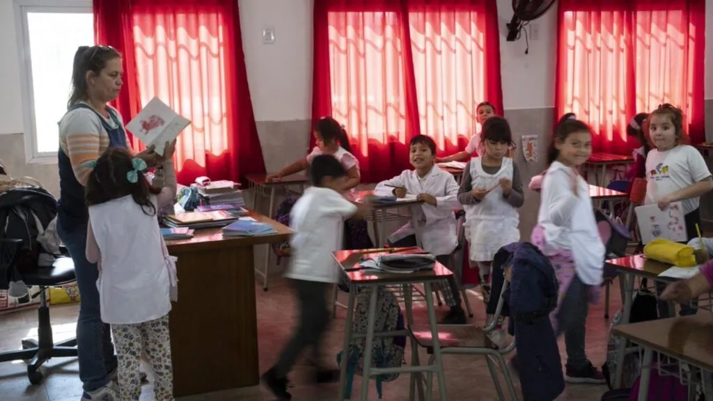 crisis educativa en Argentina con aula parcialmente vacía y estudiantes reflejando caída de matrícula y problemas de aprendizaje