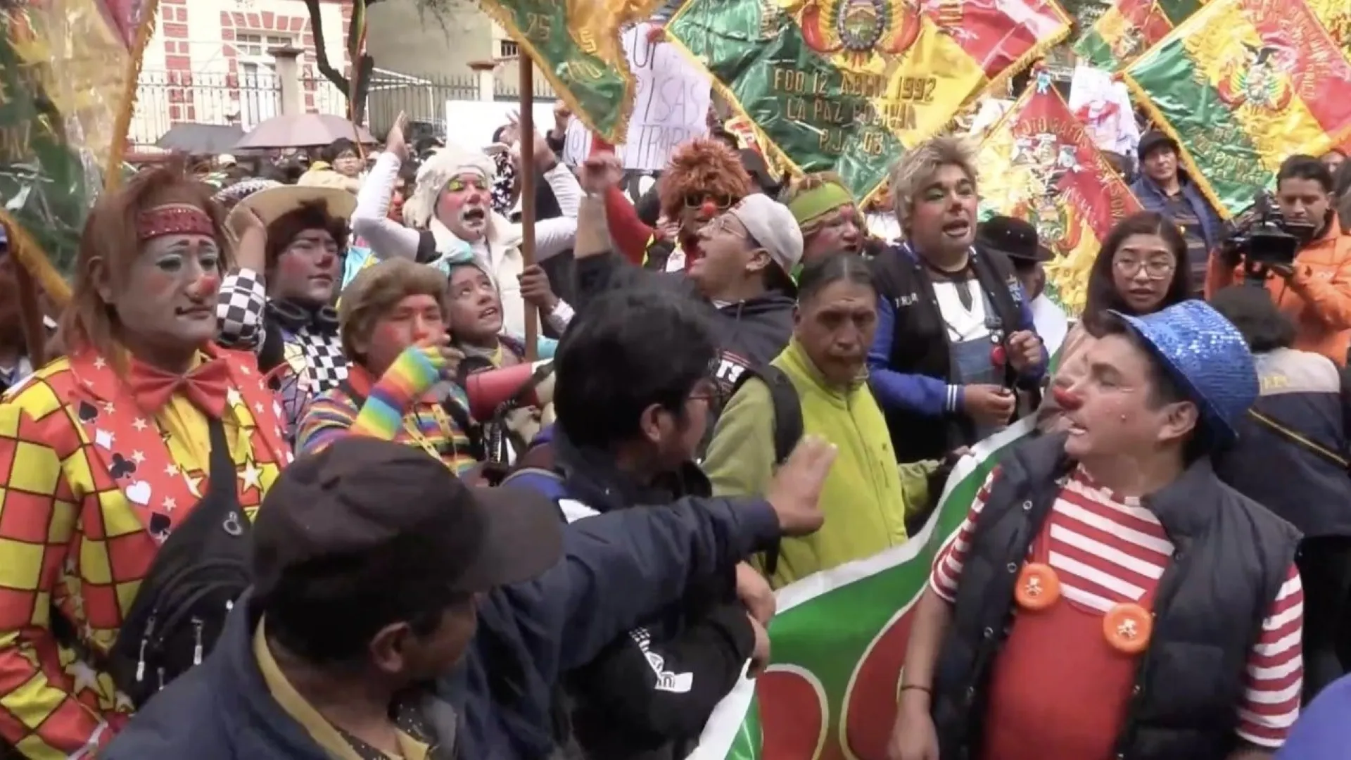 payasos de Bolivia protestando con trajes coloridos frente a institución educativa por restricciones en actividades escolares