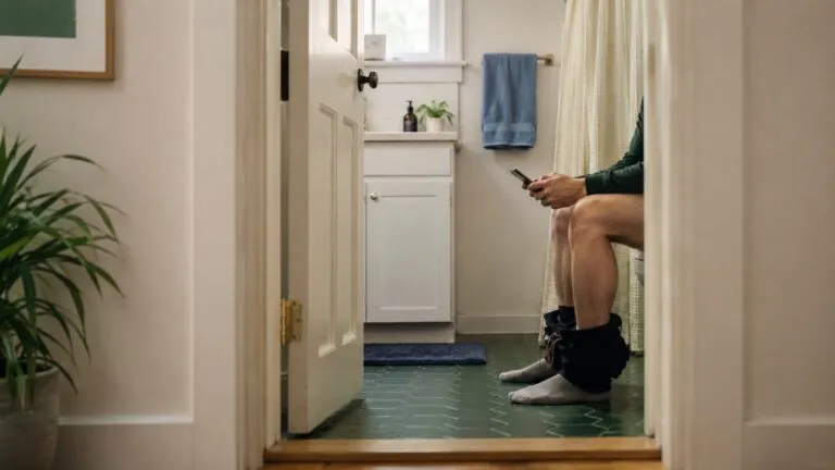 Persona utilizando un teléfono móvil en el baño, hábito relacionado con mayor riesgo de hemorroides según estudio científico.